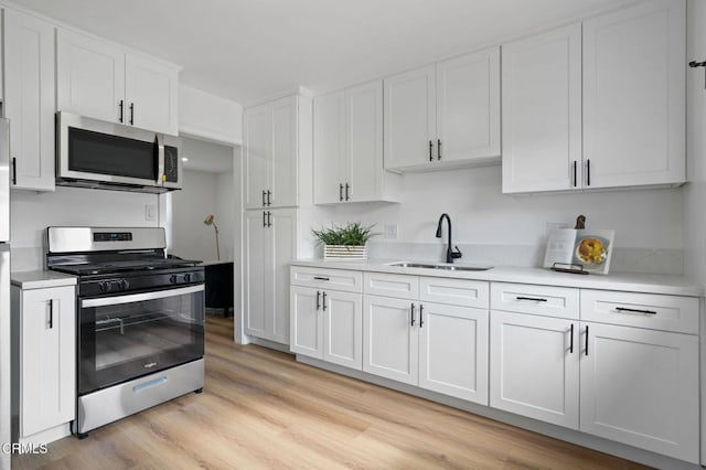 kitchen featuring white cabinets, appliances with stainless steel finishes, light countertops, light wood-type flooring, and a sink