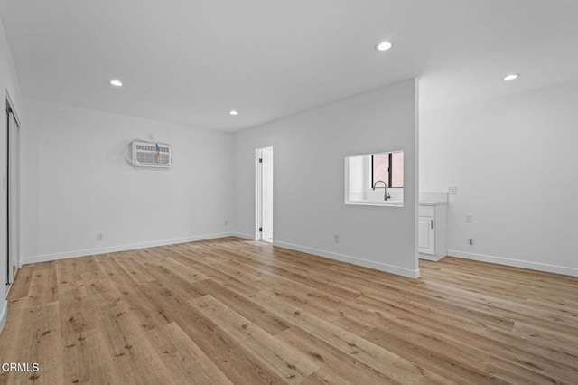 spare room with light wood-type flooring, a wall unit AC, baseboards, and recessed lighting