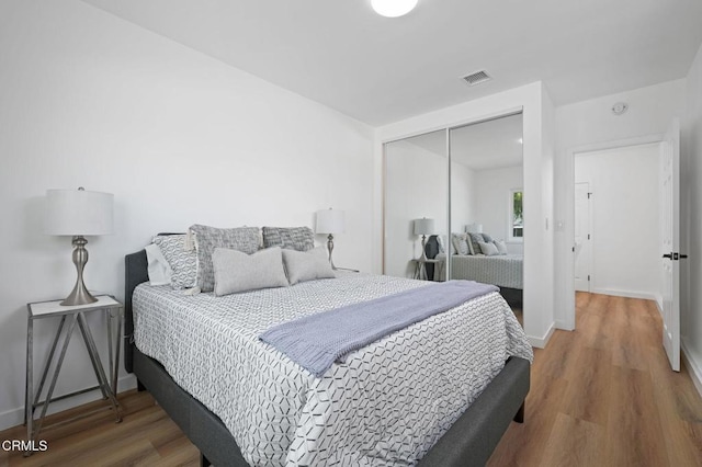 bedroom with a closet, wood finished floors, visible vents, and baseboards