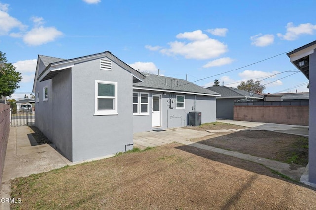 rear view of property featuring a patio, central air condition unit, fence, roof with shingles, and stucco siding