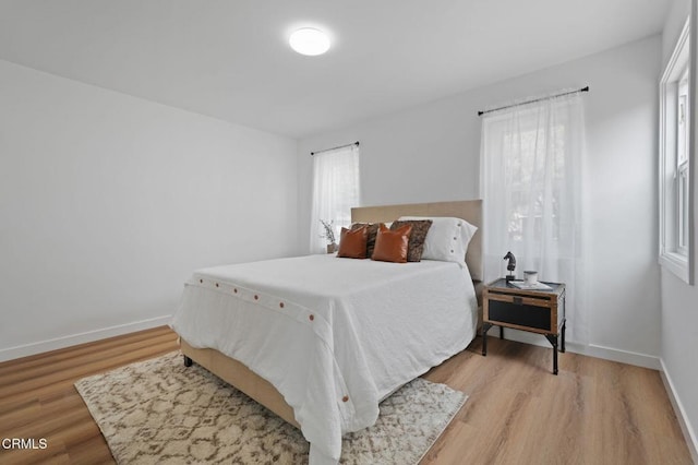 bedroom featuring multiple windows, light wood-type flooring, and baseboards