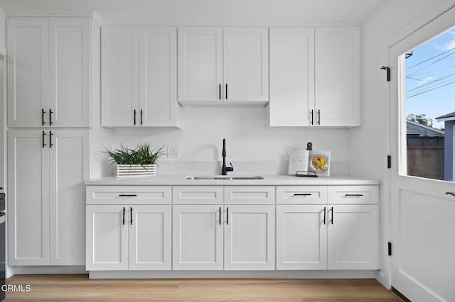 kitchen with light wood-style flooring, white cabinetry, light countertops, and a sink