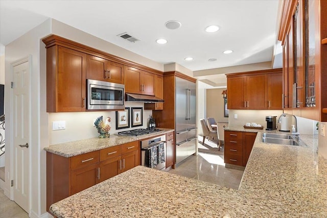 kitchen featuring stainless steel appliances, visible vents, a sink, light stone countertops, and under cabinet range hood