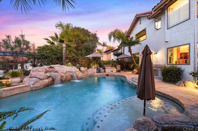 pool at dusk with an outdoor pool, a patio, and fence