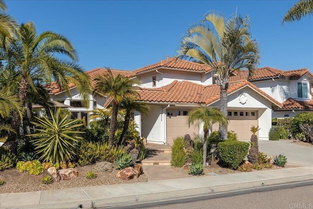 mediterranean / spanish home featuring an attached garage, driveway, a tile roof, and stucco siding