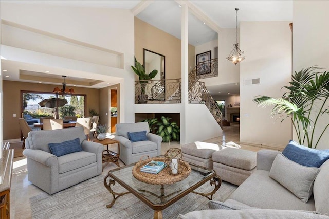 living room with high vaulted ceiling, a notable chandelier, visible vents, a lit fireplace, and a raised ceiling