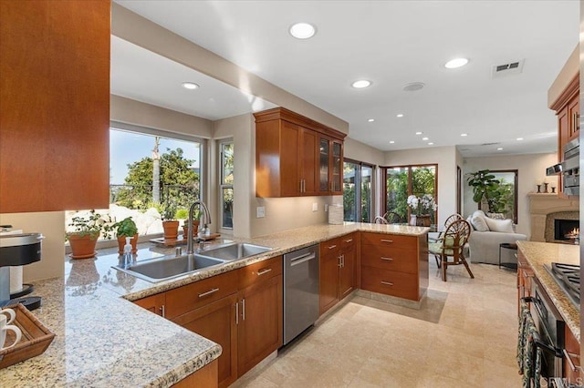 kitchen featuring a peninsula, a sink, a lit fireplace, appliances with stainless steel finishes, and glass insert cabinets