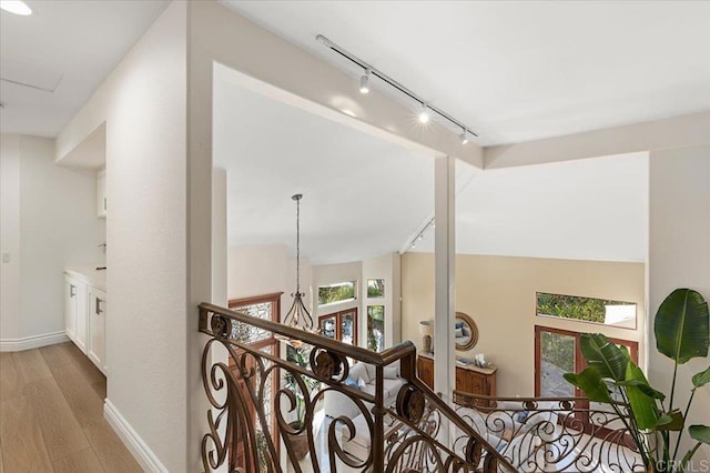 hall featuring lofted ceiling, baseboards, and light wood finished floors