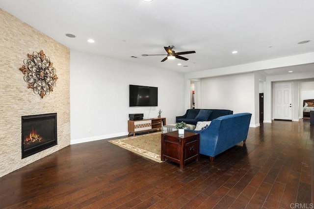 living area featuring ceiling fan, a stone fireplace, wood finished floors, and baseboards