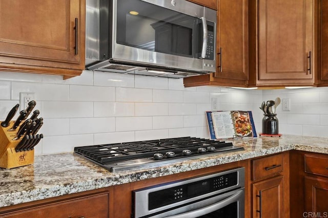 kitchen featuring appliances with stainless steel finishes, brown cabinets, decorative backsplash, and light stone countertops