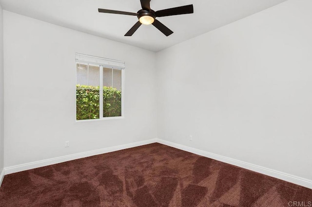 empty room featuring dark colored carpet, a ceiling fan, and baseboards