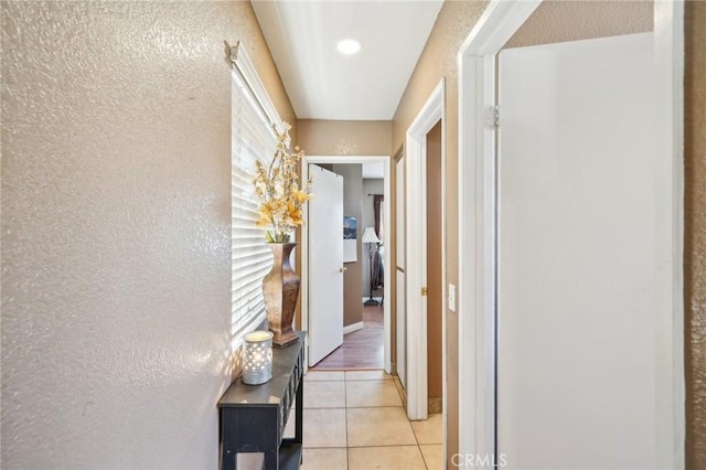 hall featuring a textured wall and light tile patterned floors