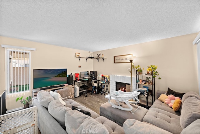 living area with a textured ceiling, a brick fireplace, and wood finished floors