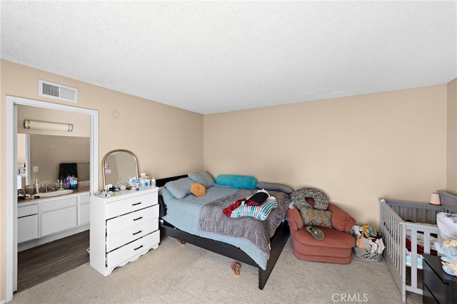 bedroom with light carpet, visible vents, a sink, and a textured ceiling