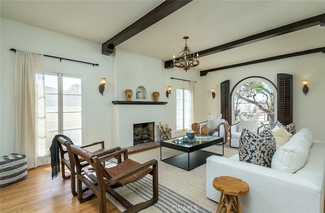 living area with a fireplace with raised hearth, beamed ceiling, light wood-style flooring, and an inviting chandelier