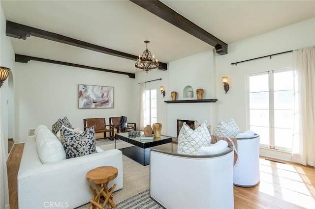 living area featuring an inviting chandelier, light wood-style flooring, a fireplace, and beamed ceiling