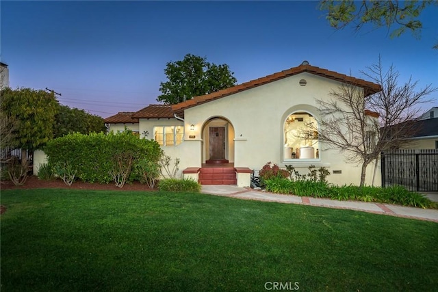 mediterranean / spanish-style house with a tiled roof, a front yard, fence, and stucco siding