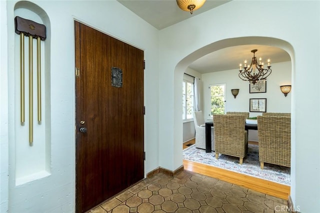 foyer entrance with arched walkways, baseboards, and a notable chandelier