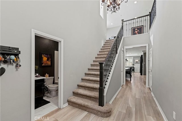 stairs featuring a chandelier, a high ceiling, baseboards, and wood finished floors