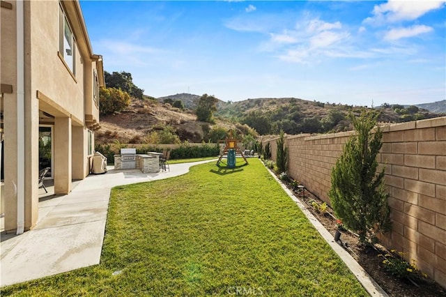 view of yard with a playground, a patio, area for grilling, a mountain view, and a fenced backyard