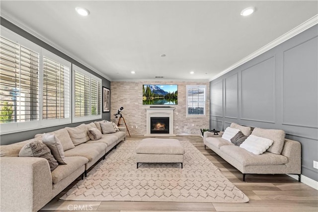 living area featuring ornamental molding, wood finished floors, a lit fireplace, a decorative wall, and recessed lighting