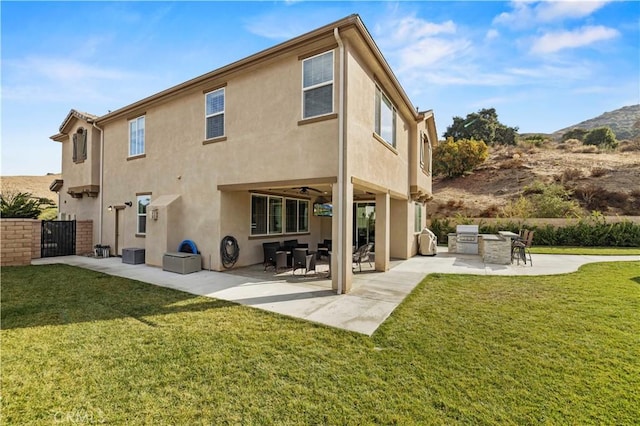 back of house with stucco siding, a lawn, exterior kitchen, and a patio