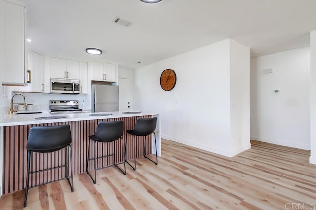 kitchen with stainless steel appliances, a sink, white cabinetry, light countertops, and light wood-type flooring