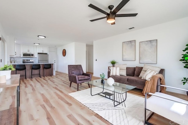 living room with ceiling fan, light wood finished floors, visible vents, and baseboards