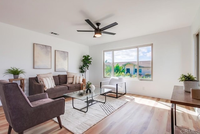 living room featuring ceiling fan, light wood-style flooring, visible vents, and baseboards