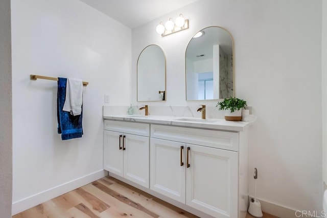 bathroom with double vanity, baseboards, a sink, and wood finished floors