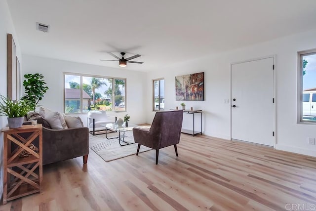 living room with light wood finished floors, baseboards, visible vents, and a ceiling fan