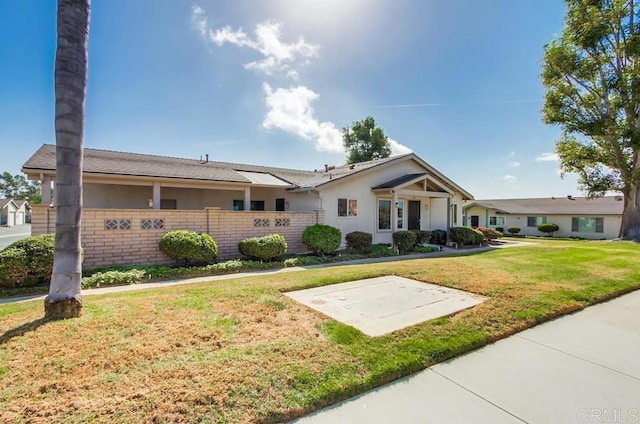 ranch-style home with brick siding, fence, stucco siding, and a front yard