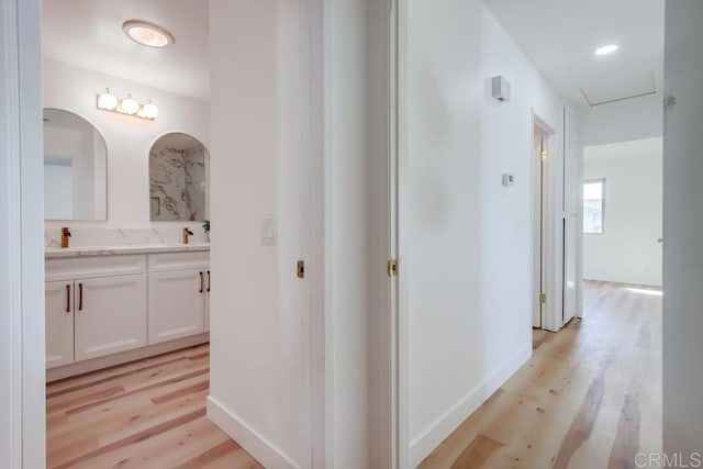 hall with light wood-type flooring, baseboards, and a sink