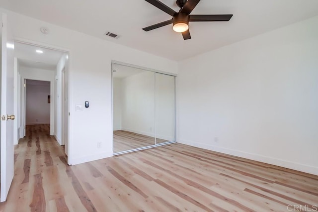 unfurnished bedroom featuring baseboards, visible vents, ceiling fan, light wood-style floors, and a closet