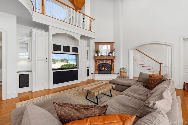 living area featuring light wood finished floors, a warm lit fireplace, arched walkways, a high ceiling, and stairs