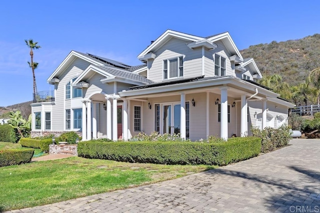 view of front of house with a garage, covered porch, solar panels, and a front yard