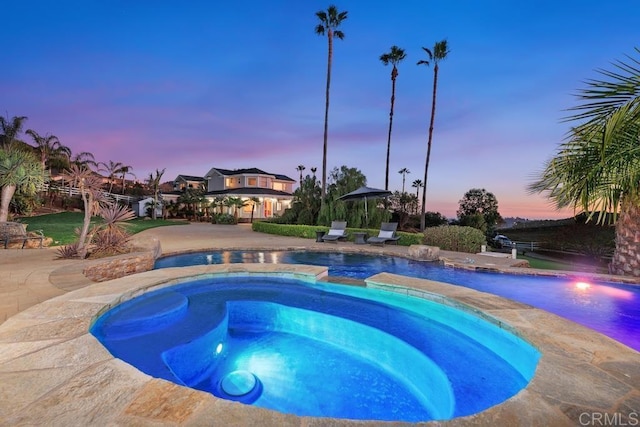 pool at dusk featuring a pool with connected hot tub