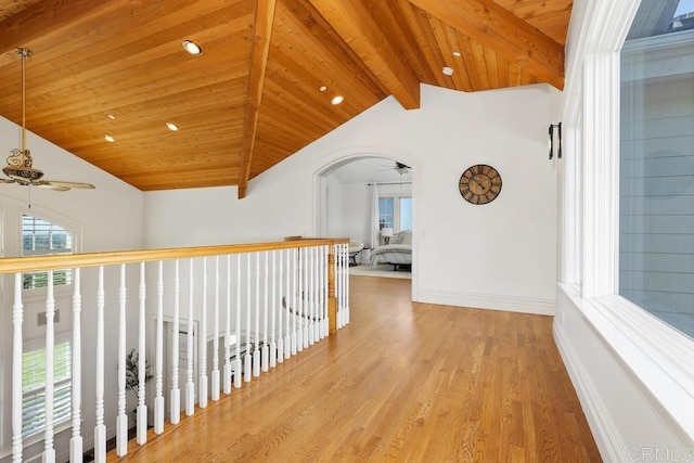 corridor featuring lofted ceiling with beams, arched walkways, wooden ceiling, light wood-style flooring, and baseboards