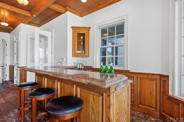 bar with brick floor, crown molding, wood ceiling, wainscoting, and wet bar