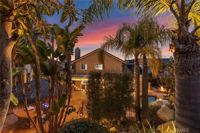 property exterior at dusk with a chimney and stucco siding