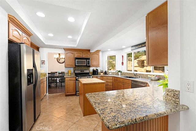 kitchen featuring a peninsula, a sink, appliances with stainless steel finishes, a center island, and a tray ceiling