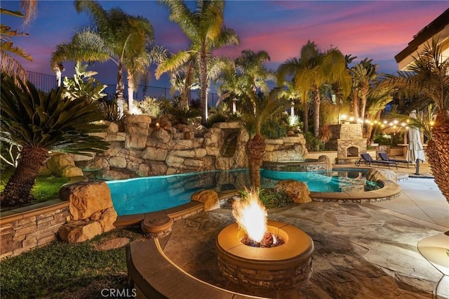 pool at dusk with an outdoor fire pit, a fenced in pool, a patio, fence, and an outdoor stone fireplace