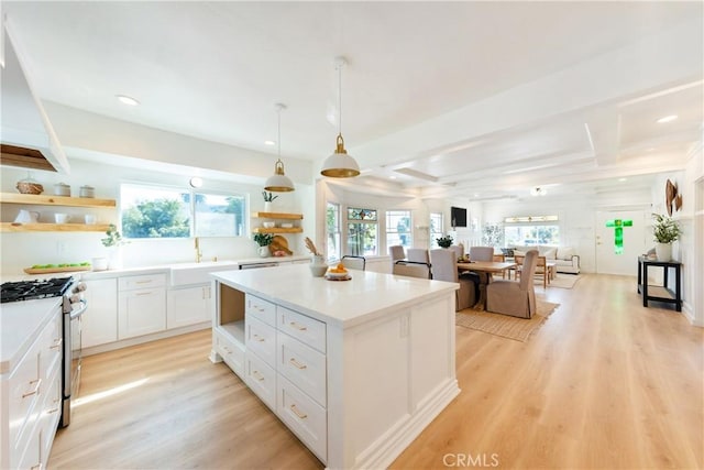 kitchen with open shelves, light countertops, white cabinets, a kitchen island, and stainless steel gas range