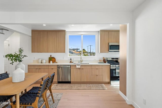 kitchen with stainless steel appliances, a sink, light wood-style flooring, and modern cabinets