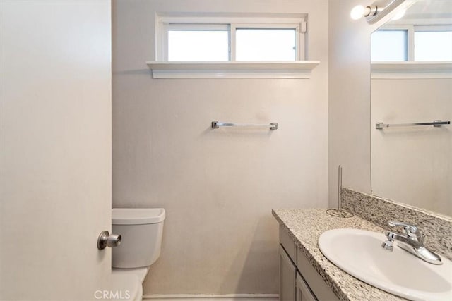 half bathroom featuring toilet, vanity, and a wealth of natural light