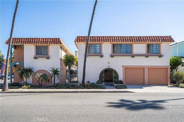 mediterranean / spanish-style house with an attached garage, fence, a tile roof, driveway, and stucco siding