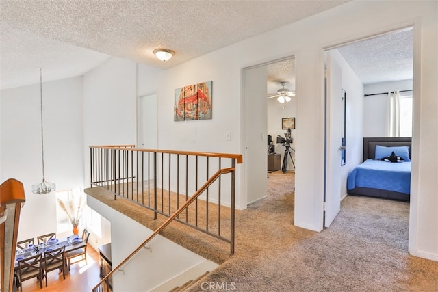 hall featuring carpet flooring, a textured ceiling, an upstairs landing, a chandelier, and baseboards