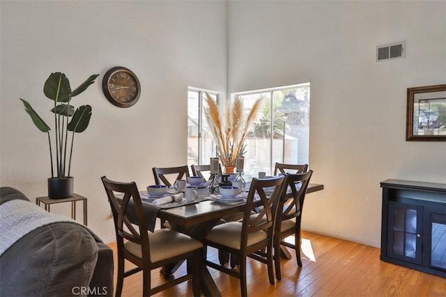 dining space featuring wood-type flooring, a towering ceiling, and visible vents