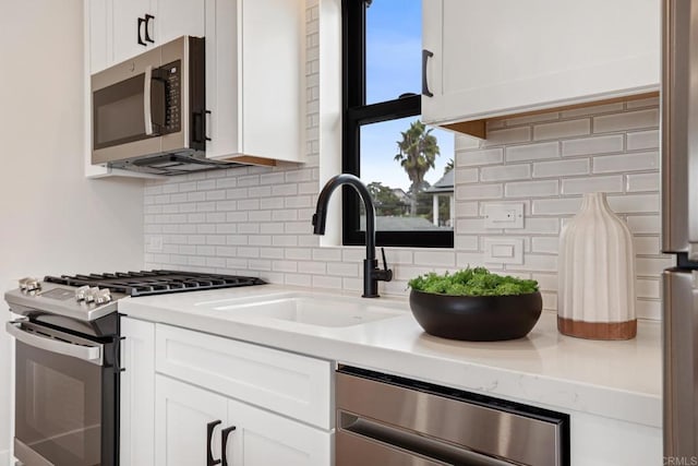 kitchen with decorative backsplash, appliances with stainless steel finishes, white cabinets, and a sink