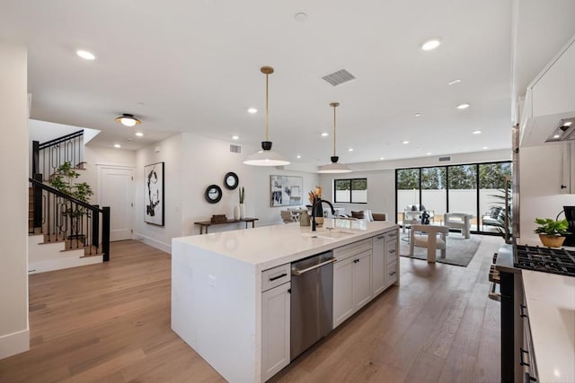 kitchen with a center island with sink, light countertops, visible vents, stainless steel dishwasher, and white cabinets